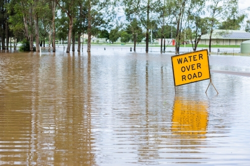 Floodwater rising over water over road sign on highway - Australian Stock Image
