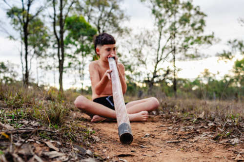 Focus on didgeridoo boy is playing in Australian bushland - Australian Stock Image
