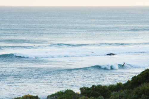 focus on horizon in foreground a lone surfer riding a wave - Australian Stock Image