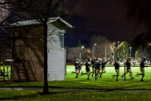 Football team running laps around an oval on a winters night - Australian Stock Image