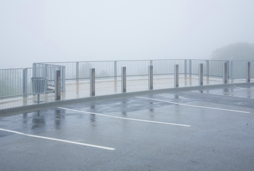 Footpath, railing and empty car park in mist and rain