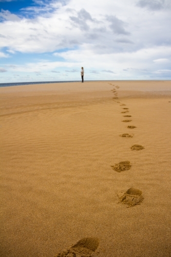 Footprints on a beach leading to a person in the distance