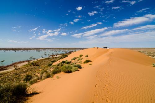 Footprints on a sand dune leading to a man and a vehicle with lake below and cloud formations - Australian Stock Image