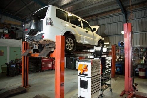Four wheel drive lifted in hoist for repairs in a mechanic workshop - Australian Stock Image