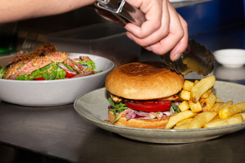 Fresh cooked chicken burger with salad and chips for lunch with salmon and salad in the background - Australian Stock Image