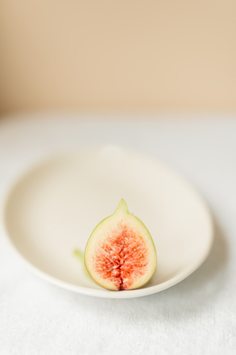 Fresh fig fruit cut in half on plain white plate - Australian Stock Image