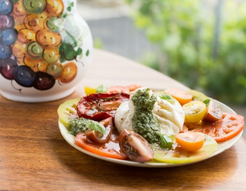 Fresh multi coloured tomato salad with buffalo mozzarella and green basil pesto, on an outdoor table