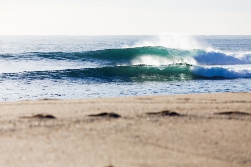 Fresh ocean waves breaking in bright morning light towards a beautiful sandy beach with footprints - Australian Stock Image