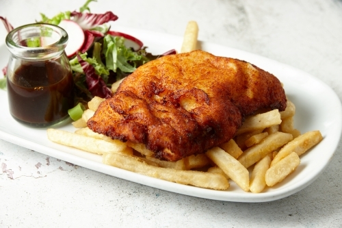 Fried meat on French fries and salad - Australian Stock Image