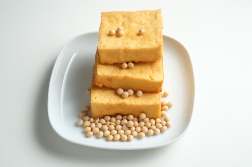 Fried tofu served in a white plate with soybeans. - Australian Stock Image