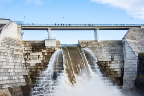 Full weir flowing with water while people view from over head. - Australian Stock Image
