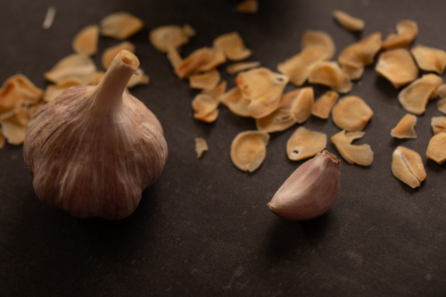 Garlic bulb with clove and garlic chips on dark benchtop - Australian Stock Image