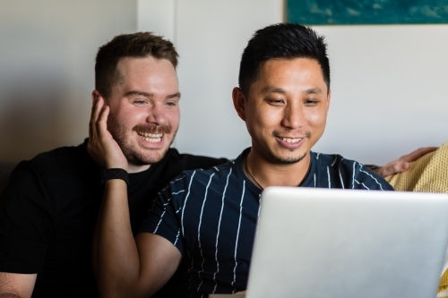 Gay couple on sofa with laptop - Australian Stock Image