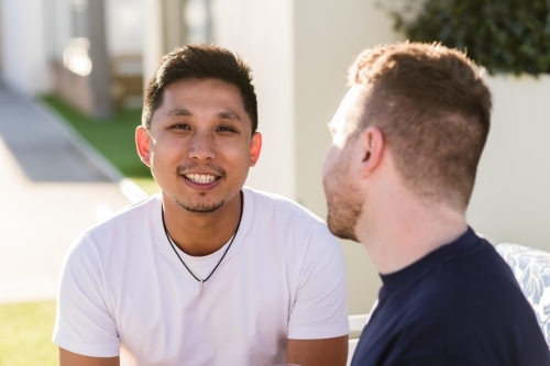 Gay couple sitting outside, mixed race - Australian Stock Image