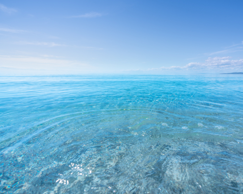 Gentle ripples shimmer across crystal-clear turquoise water beneath a cloudless summer sky - Australian Stock Image