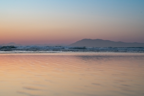 Gentle waves ripples on the surface of the ocean with a silhouette of a mountain range - Australian Stock Image