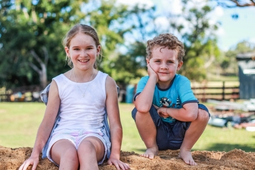 Girl and boy sitting on pile of dirt - Australian Stock Image