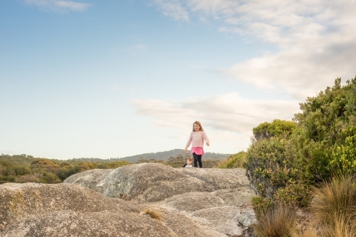 Girl and boy walking over boulder rocks - Australian Stock Image