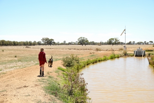 Girl and dog walking along channel bank on farm - Australian Stock Image
