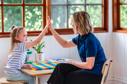 Girl and speech therapist high five in clinic in celebration - Australian Stock Image