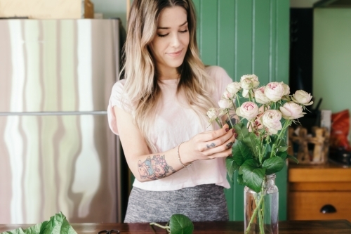 Girl arranging pink roses in a glass jar vase in her kitchen - Australian Stock Image