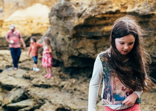 Girl carrying shells, family in background. Exploring limestone beach - Australian Stock Image