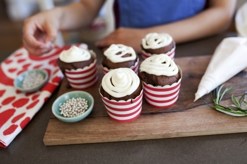 Girl decorating christmas cupcakes in kitchen at home - Australian Stock Image