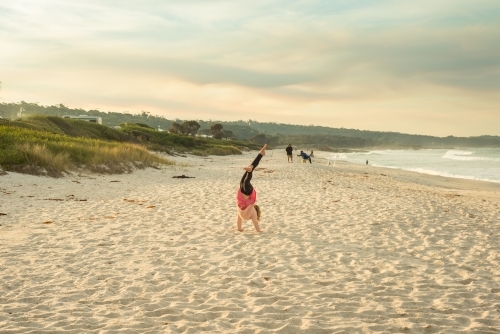 Girl doing cartwheels on a beach at sunset
