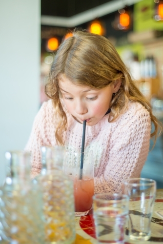 Girl drinking a red drink through a straw - Australian Stock Image