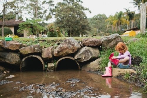Girl exploring a stormwater drain in gumboots - Australian Stock Image