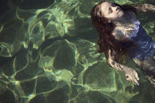 Girl floating on her back in sunlit water - Australian Stock Image