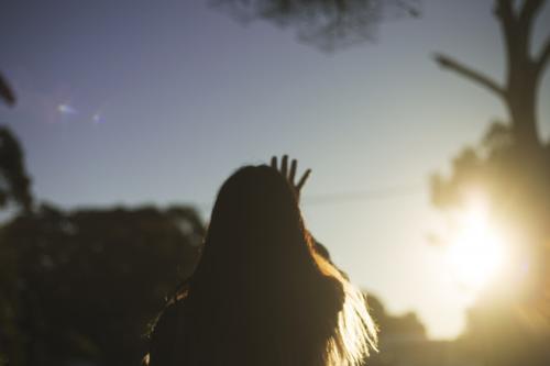 Girl from behind reaching out to setting sun