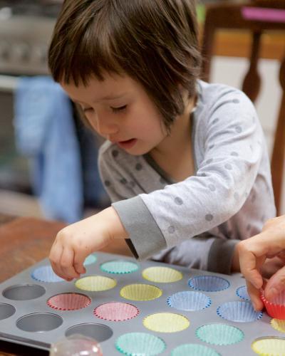 Girl helping bake cupcakes by putting patty pans in a baking tin - Australian Stock Image