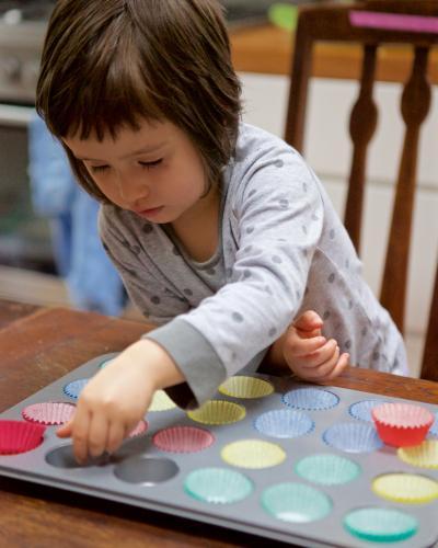 Girl helping bake cupcakes by putting patty pans in a baking tin - Australian Stock Image