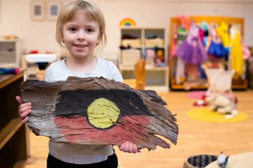 Girl holding painted Aboriginal flag on tree bark - Australian Stock Image