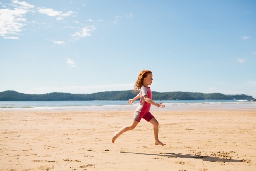 Girl in a wetsuit running on the sand at the beach - Australian Stock Image