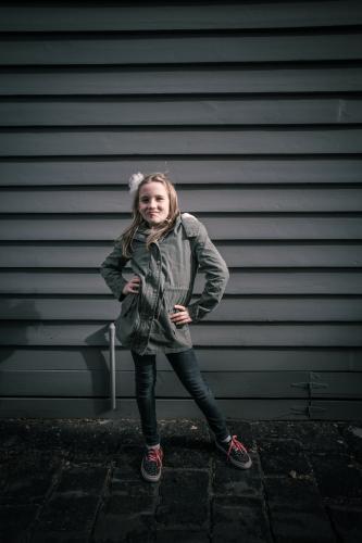 Girl in grey standing in front of grey weatherboards in the city - Australian Stock Image