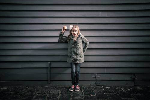 Girl in grey standing in front of grey weatherboards in the city holding an apple