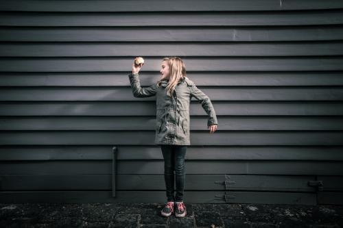 Girl in grey standing in front of grey weatherboards in the city holding an apple