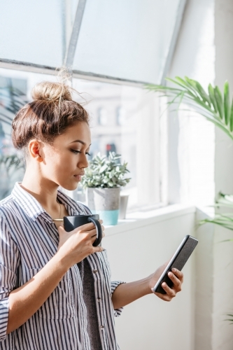 Girl in her 20s looking at her phone with a coffee in the morning sunshine - Australian Stock Image