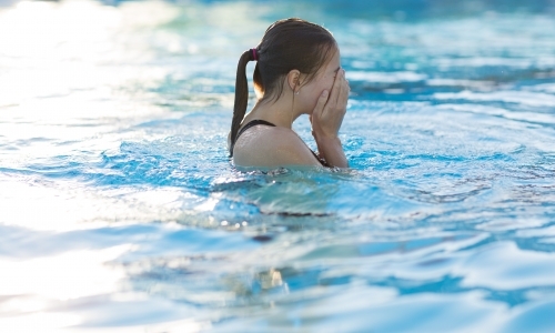 Girl in swimming pool wiping eyes - Australian Stock Image
