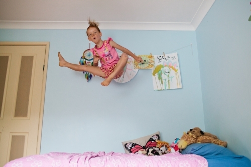 Girl jumping high on a bed - Australian Stock Image