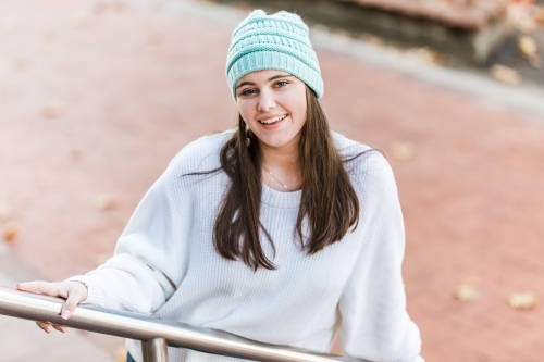Girl leaning against hand rail smiling wearing beanie - Australian Stock Image