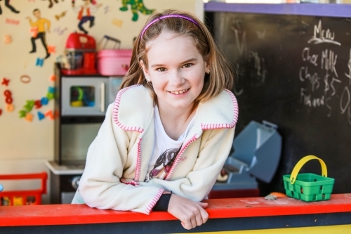 Girl leaning on bench of cubby house smiling - Australian Stock Image