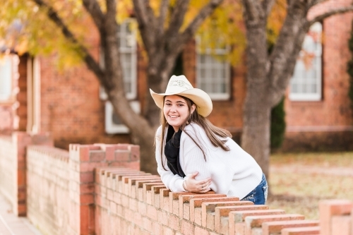 Girl leaning on brick wall near building smiling in hat and scarf - Australian Stock Image