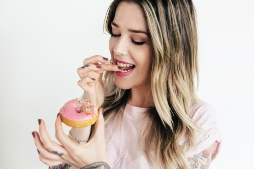 Girl licking her finger and about to eat a pink iced donut - Australian Stock Image