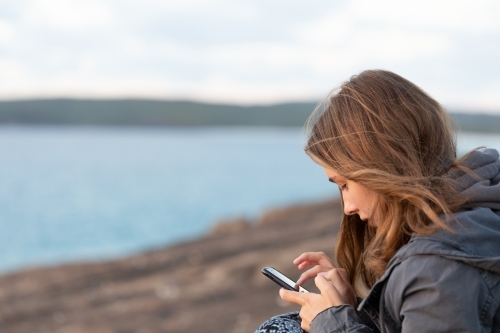 Girl looking at smartphone near the sea