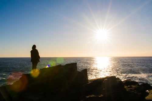 Girl looking out to sea during sunrise from a cliffside - Australian Stock Image