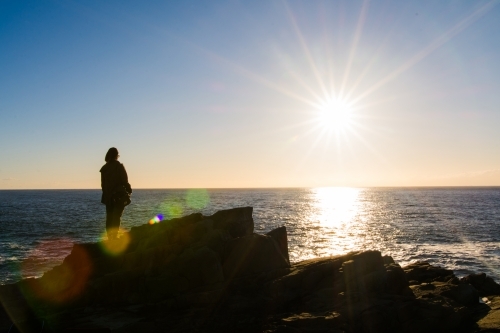 Girl looking out to sea during sunrise from a cliffside