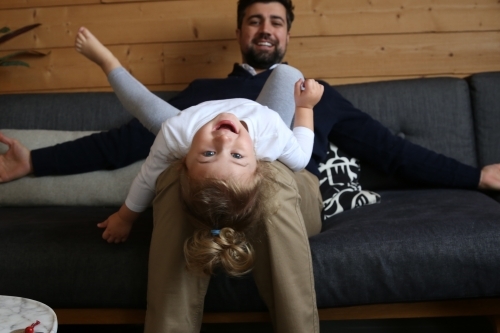 Girl lying on dad's lap on lounge - Australian Stock Image